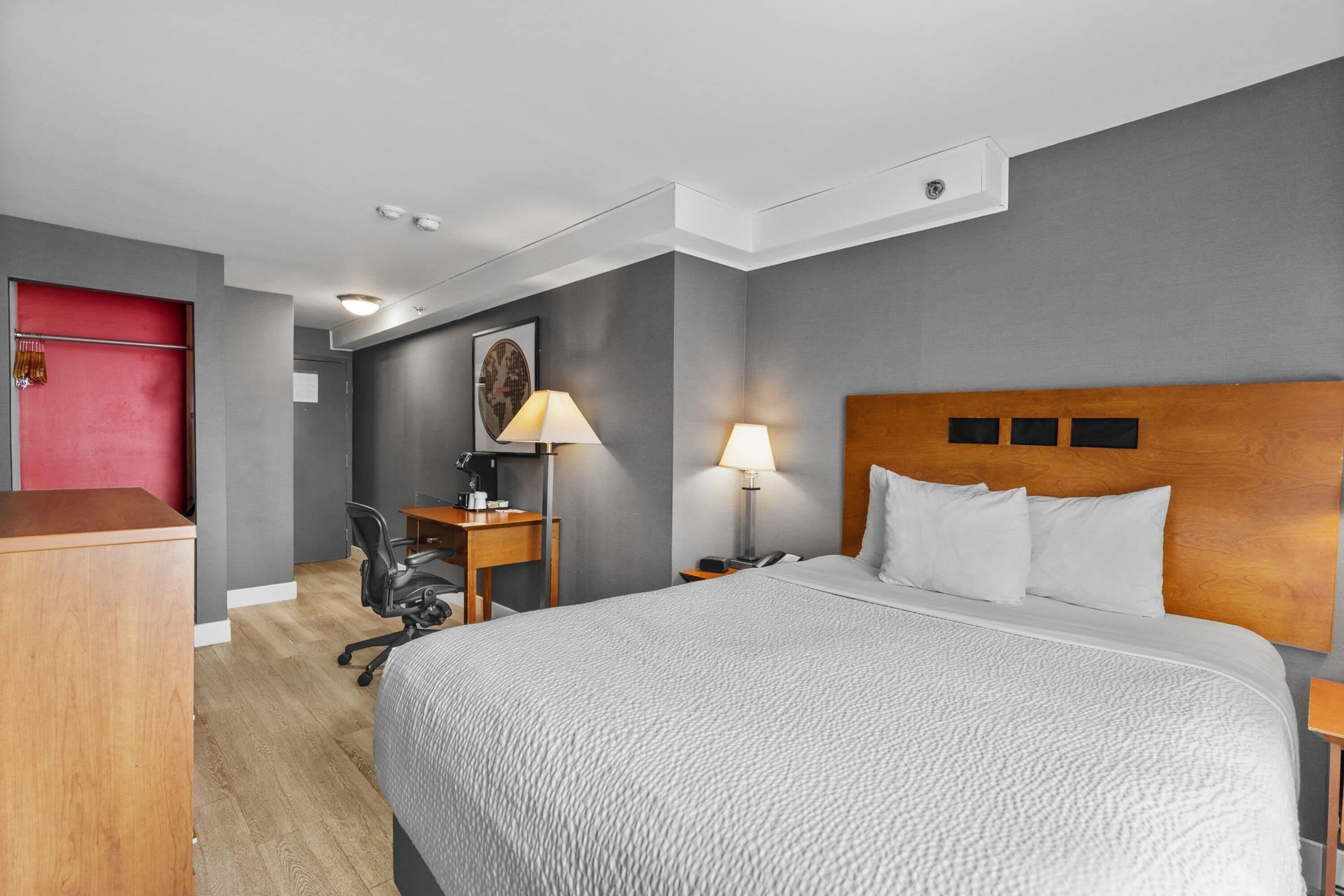A hotel room with a bed, desk, chair, and a red door.