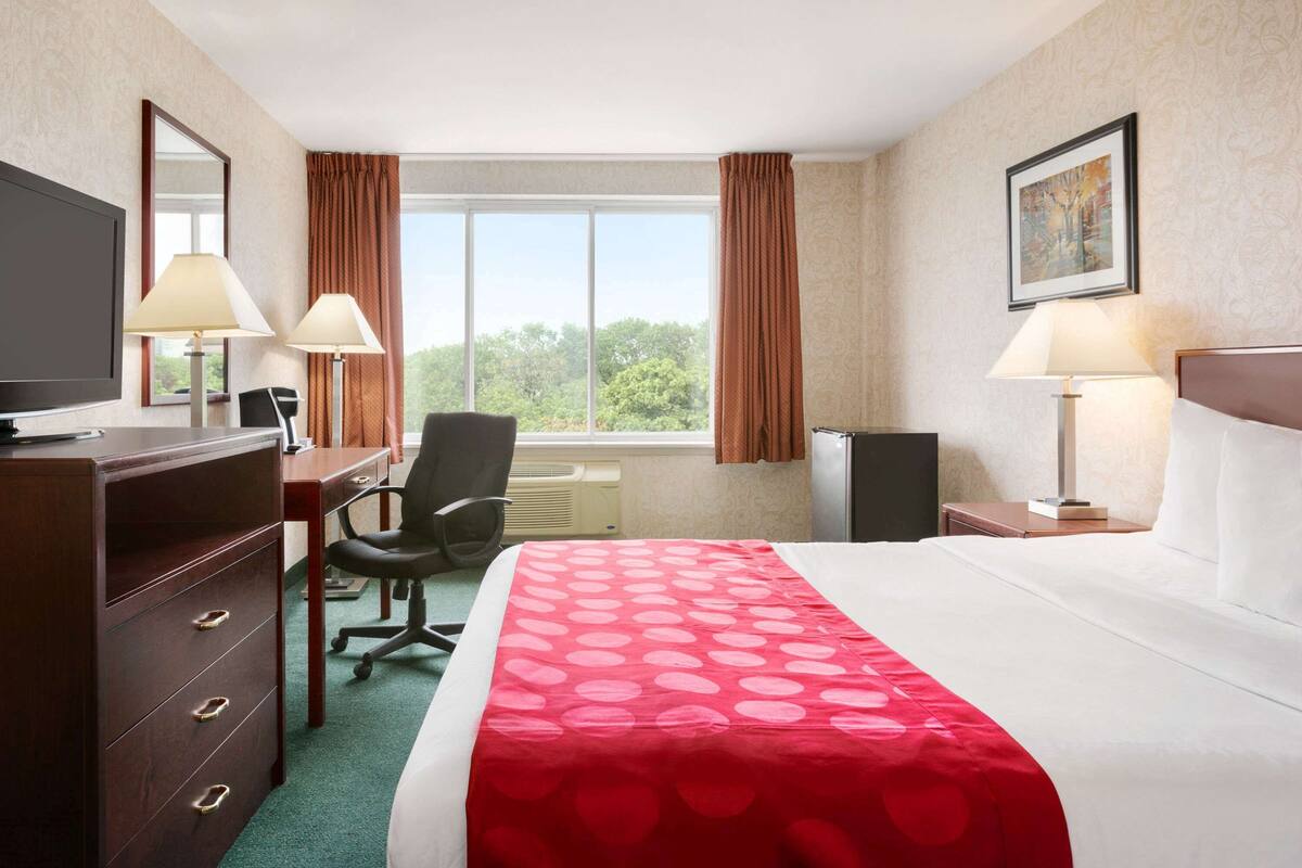 Ein Hotelzimmer mit Bett, Schreibtisch, Stuhl, Fernseher und einem Fenster mit Vorhängen.