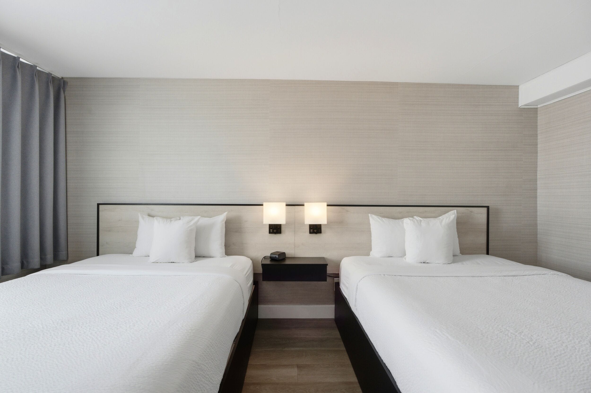 Une chambre d’hôtel avec deux lits, une table de chevet et une lampe fixée au mur.