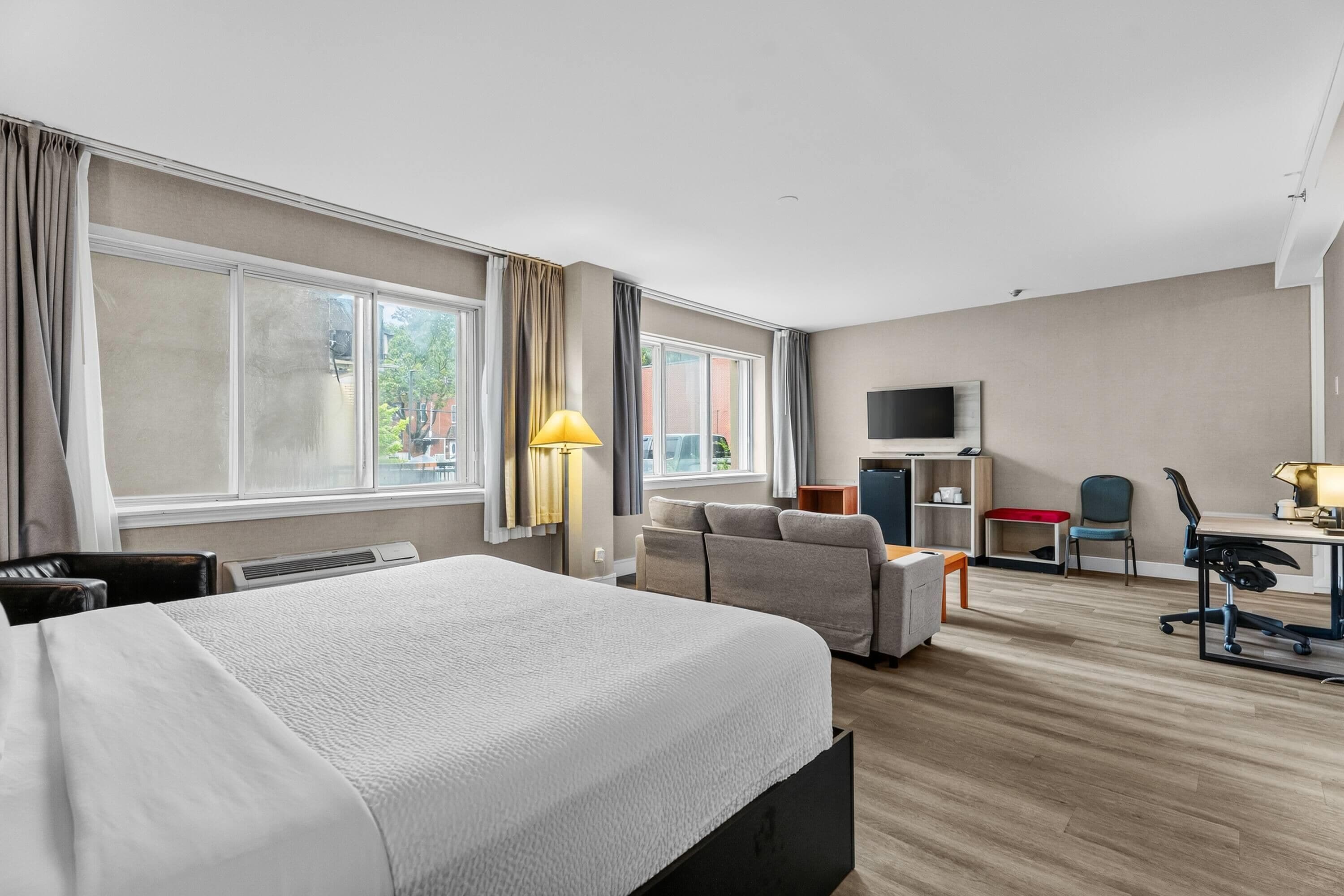 A hotel room with a bed, a desk, a chair, a TV, and large windows.