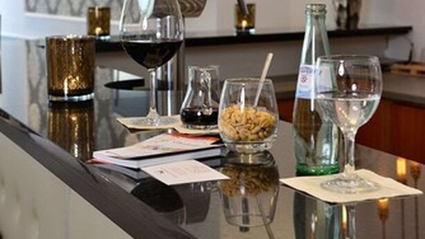 A bar area with a marble countertop, wine glasses, a bottle of water, and a coffee machine. - Hotel Celler Hof (Celle)