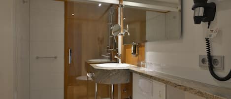 Un baño moderno con cabina de ducha de vidrio, lavamanos de mármol y secador de pelo montado en la pared.