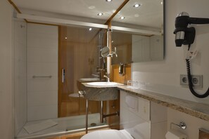 A modern bathroom with a glass shower enclosure, a marble sink, and a hairdryer mounted on the wall. - Hotel Celler Hof (Celle)