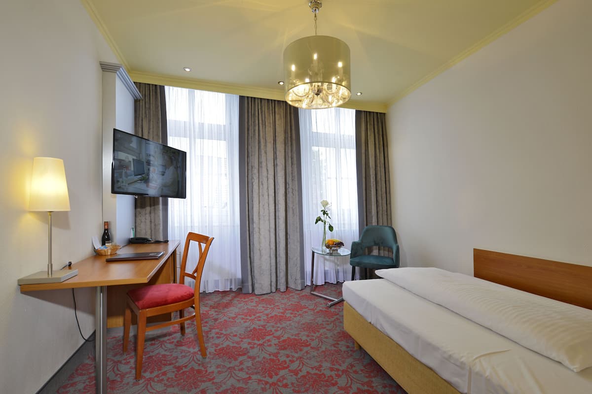 Habitación de hotel con cama, escritorio, silla, televisor y una pequeña mesa con una flor.