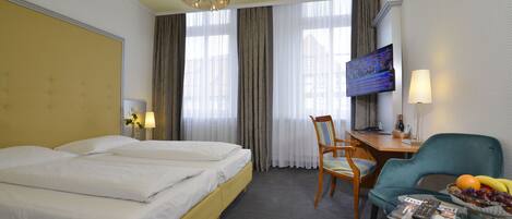 Habitación de hotel con cama doble, un escritorio con silla, televisión y un frutero sobre una mesa.