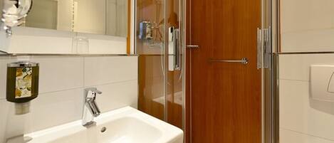 Un baño con lavamanos blanco, cabina de ducha con mampara de vidrio y puerta de madera.
