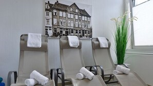 A room with three sun loungers, each with a towel. There's a large window on the right and a wall with a building illustration. - Hotel Celler Hof (Celle)