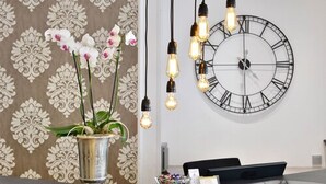 A reception area with a large wall clock, hanging light bulbs, and a potted orchid plant. - Hotel Celler Hof (Celle)