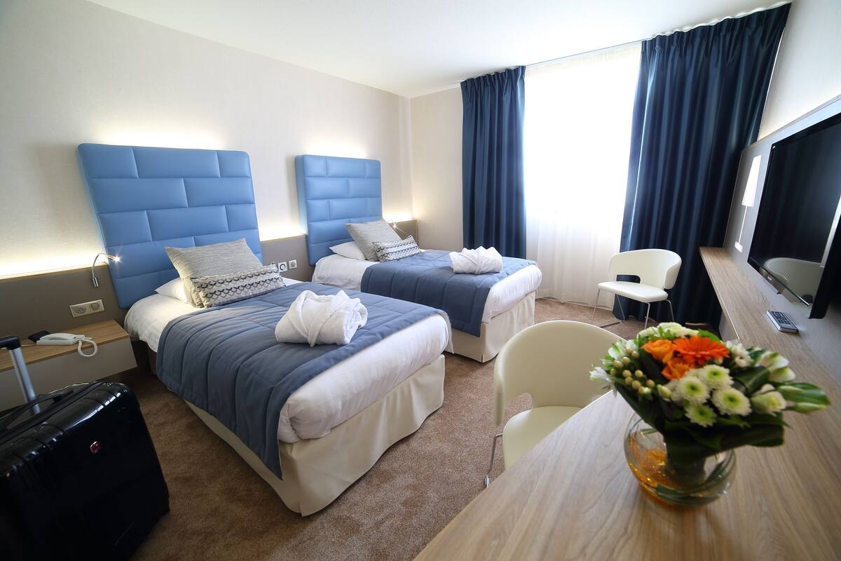 Ein Hotelzimmer mit zwei Betten, einem Schreibtisch, einem Stuhl, einem Fernseher und einer Vase mit Blumen.