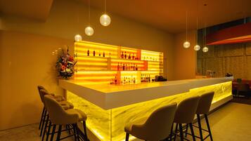 Zona bar moderna con bancone in marmo, sgabelli e un'illuminata vetrina di bottiglie.