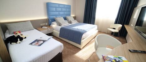 Quarto de hotel com cama, mesas de cabeceira, escrivaninha, cadeira, televisão e janela com cortinas.