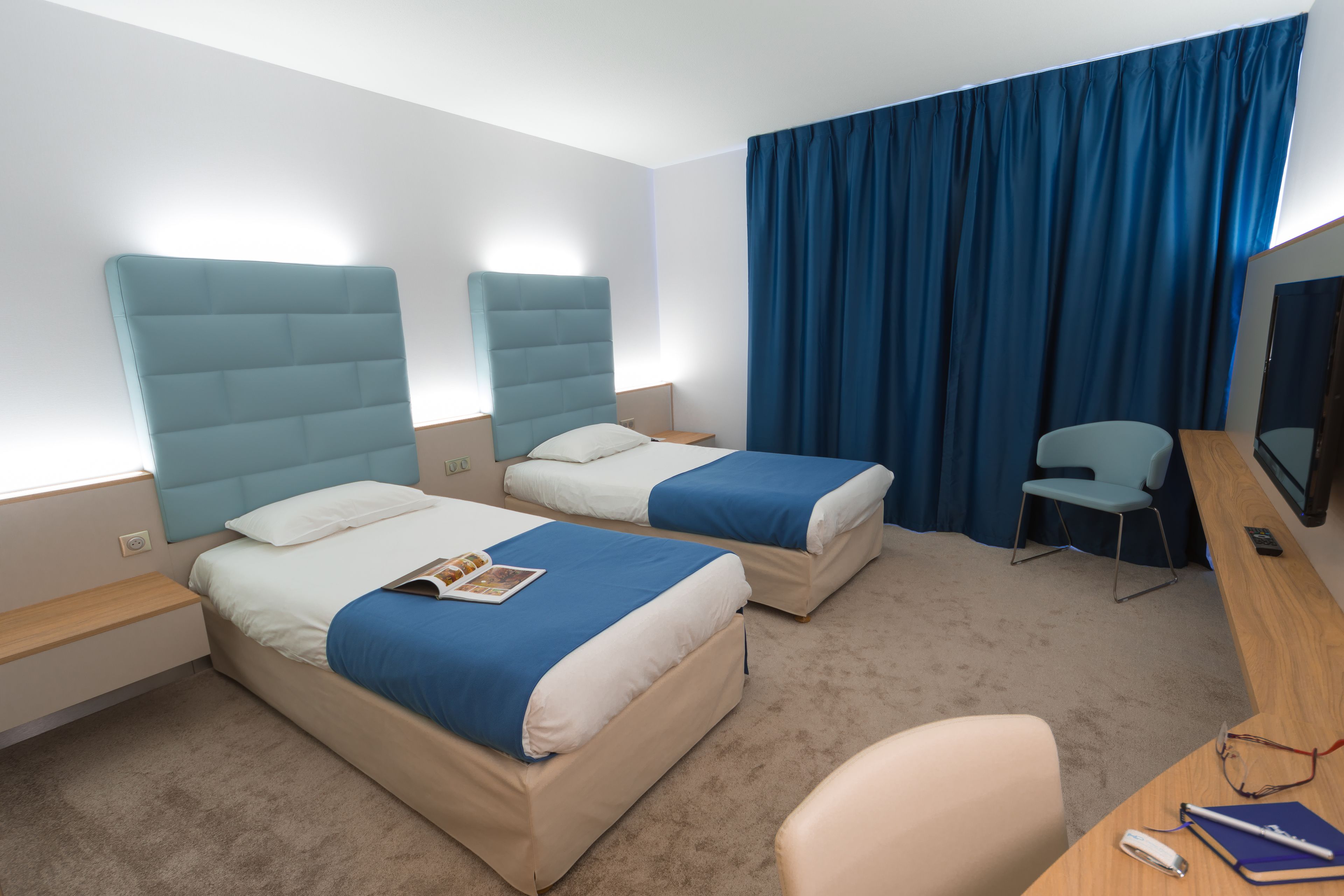 A hotel room with two beds, a desk, a chair, and a TV.