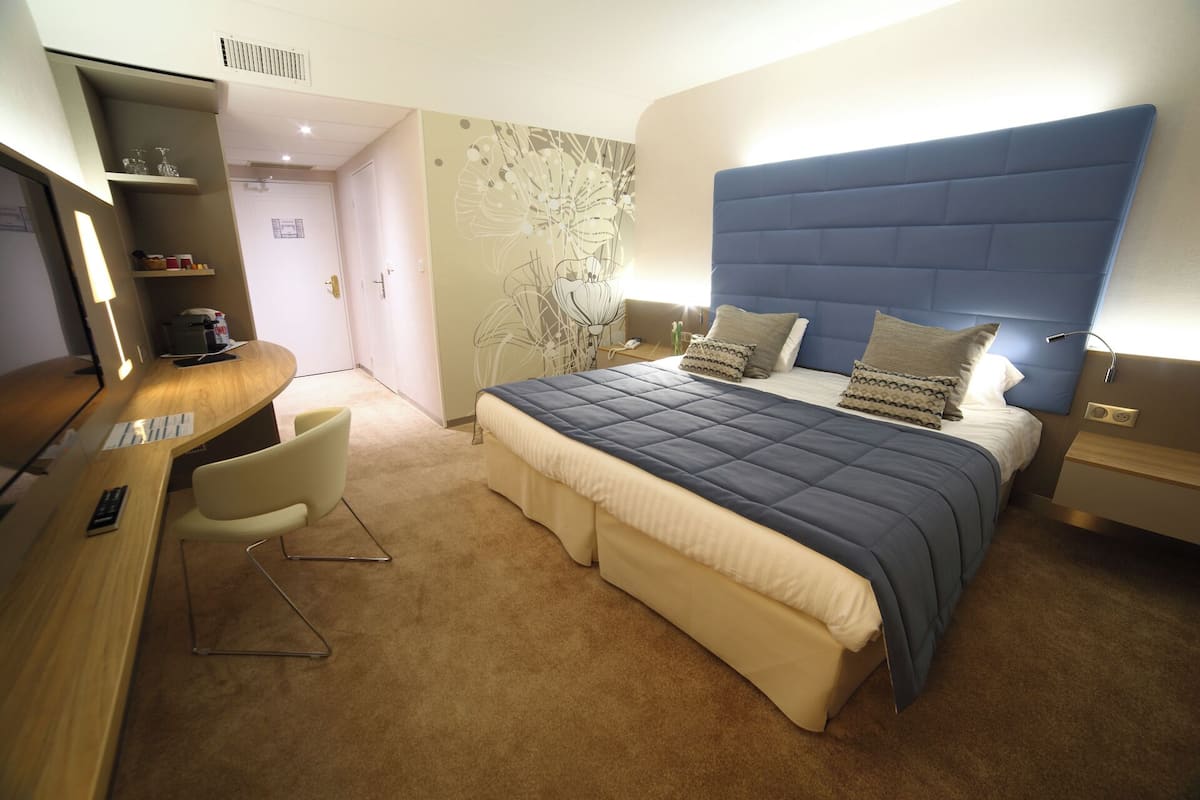 A modern hotel room with a bed, bedside tables, a desk, and a chair.