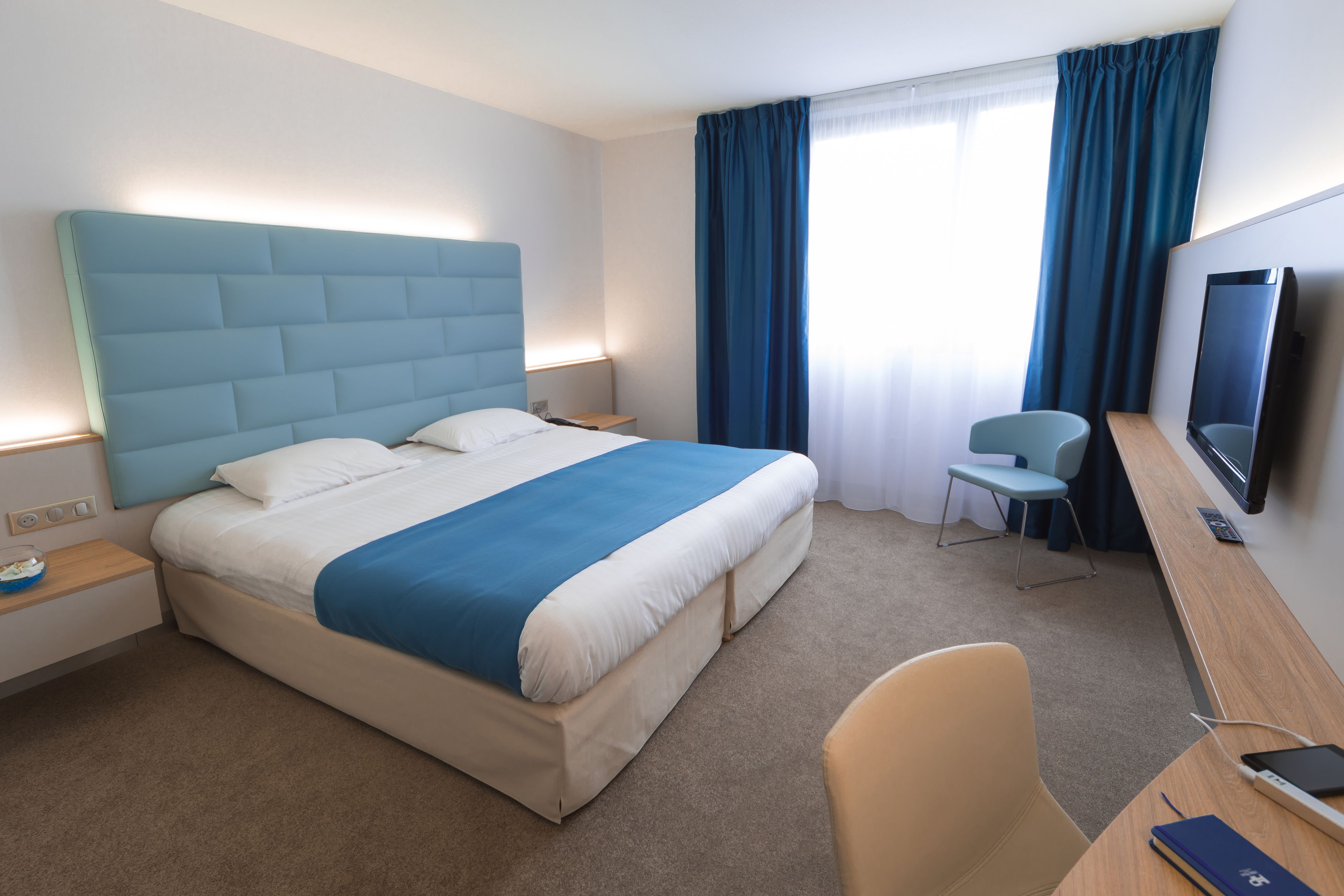 Une chambre d’hôtel moderne, dotée d’un grand lit, d’un bureau, d’une chaise, d’une télévision et d’une fenêtre avec des rideaux.