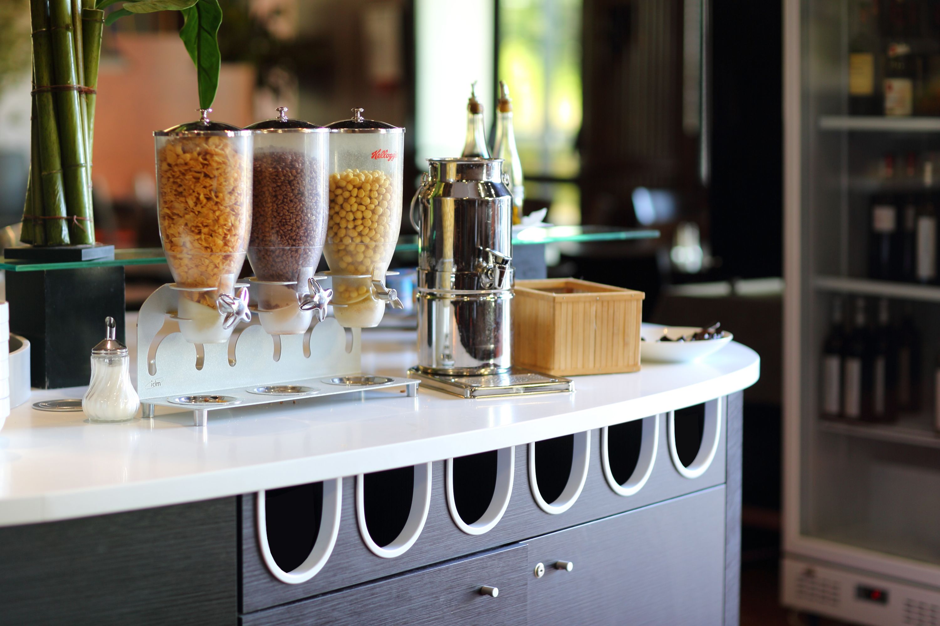 A bar area with a white countertop, three condiment dispensers, a metal coffee pot, and a small wooden box.