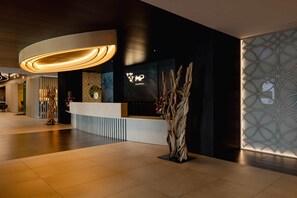 Ein moderner Hotel-Empfangsbereich mit einer Rezeption, einer großen beleuchteten Schrifttafel und einer Wand mit geometrischen Mustern.