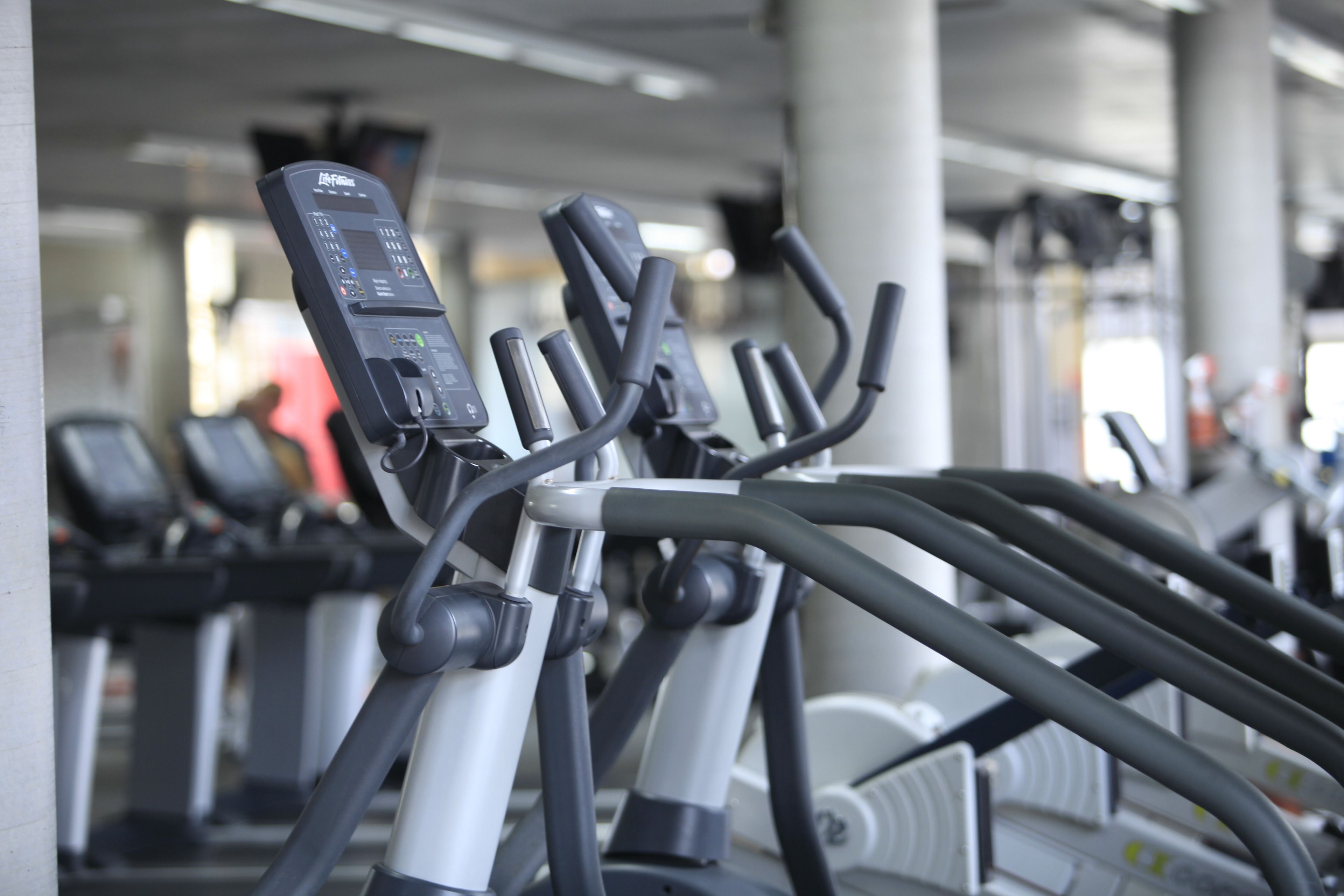 A row of stationary bikes in a gym with a concrete pillar and ceiling lights.