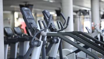 A row of stationary bikes in a gym with a concrete pillar and ceiling lights.