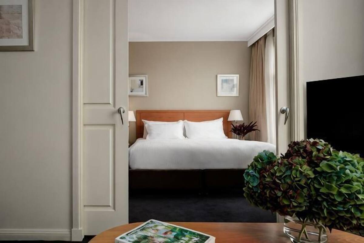 Hotellihuone, jossa on sänky, yöpöytälamput, lehti pöydällä ja ruukkukasvi.