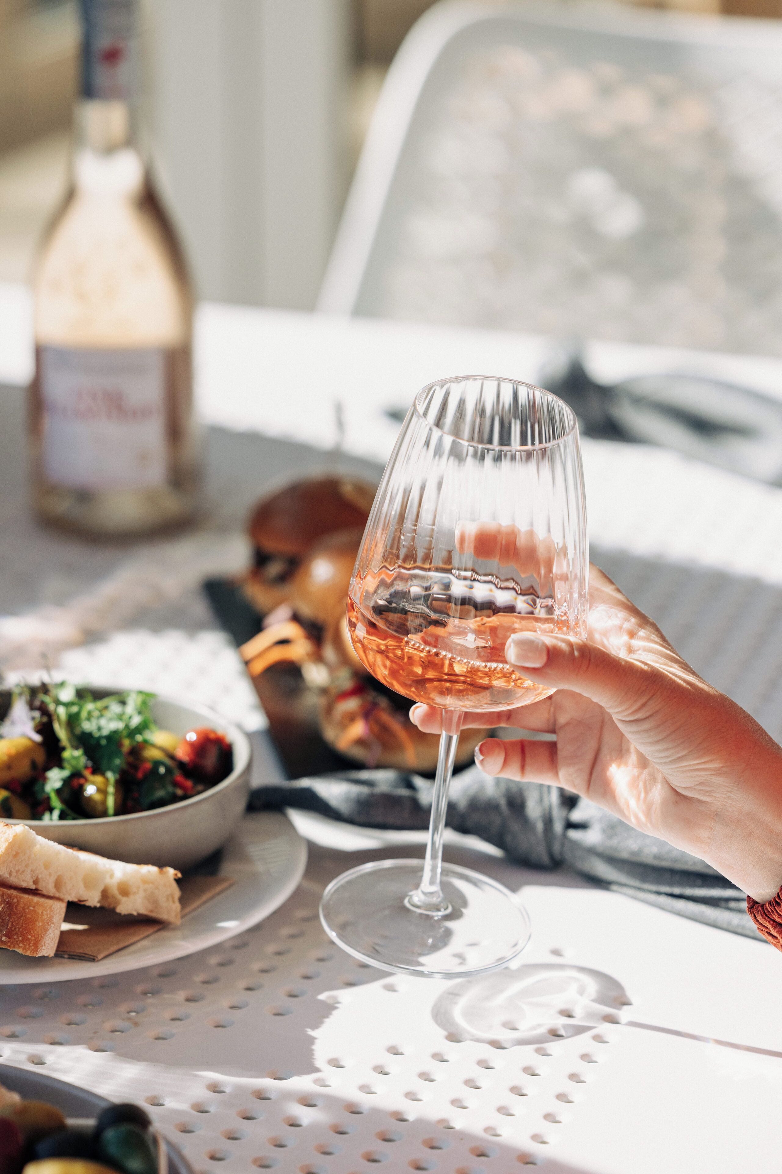 A table with a bottle of wine, a glass of wine, and a bowl of salad.