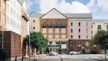 A multi-story building with a central entrance, a sign reading 'RYDGES,' and two cars parked in front.