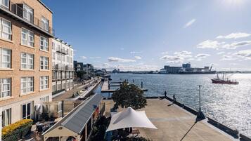 A riverside building with a patio area, a covered seating area, and a view of the river and distant cityscape.