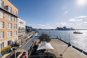 A riverside building with a patio area, a covered seating area, and a view of the river and distant cityscape.