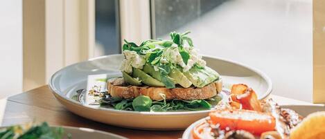 A dining table with various dishes, including a sandwich with greens and cheese, a plate with a fruit salad, and a dessert with nuts and berries.