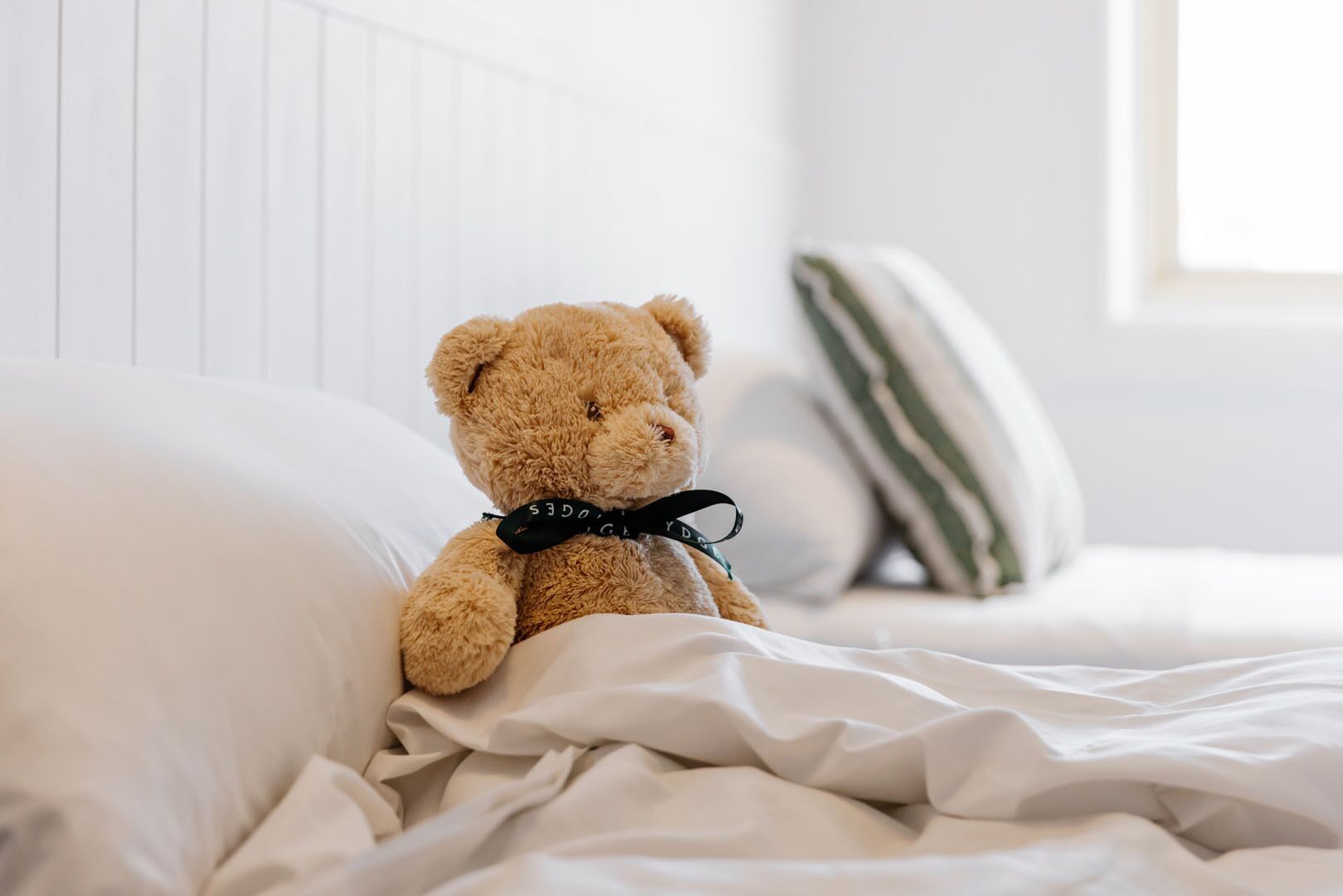 A teddy bear on a bed with white bedding and striped pillows.