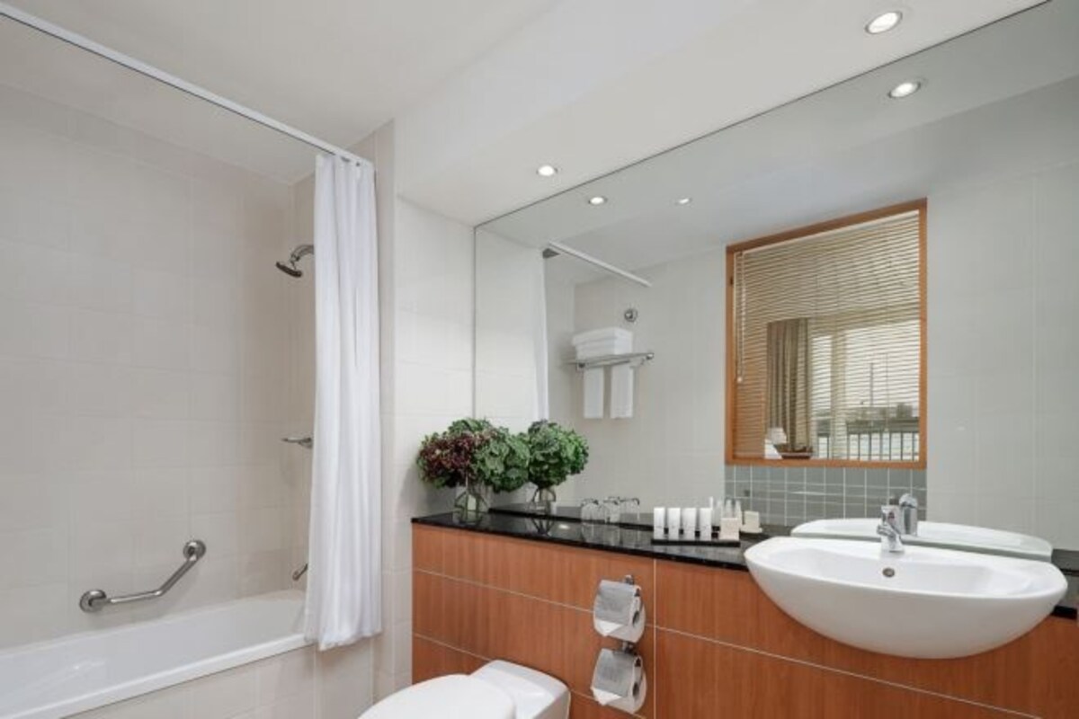 A modern bathroom with a walk-in shower, a large sink, and a mirror with a window above it.