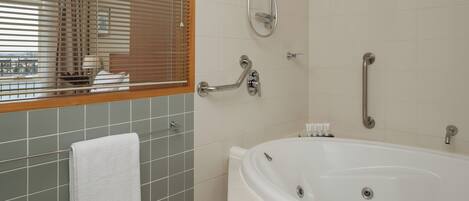 Un baño con bañera, ducha, barra de apoyo, toallero y ventana con persianas.