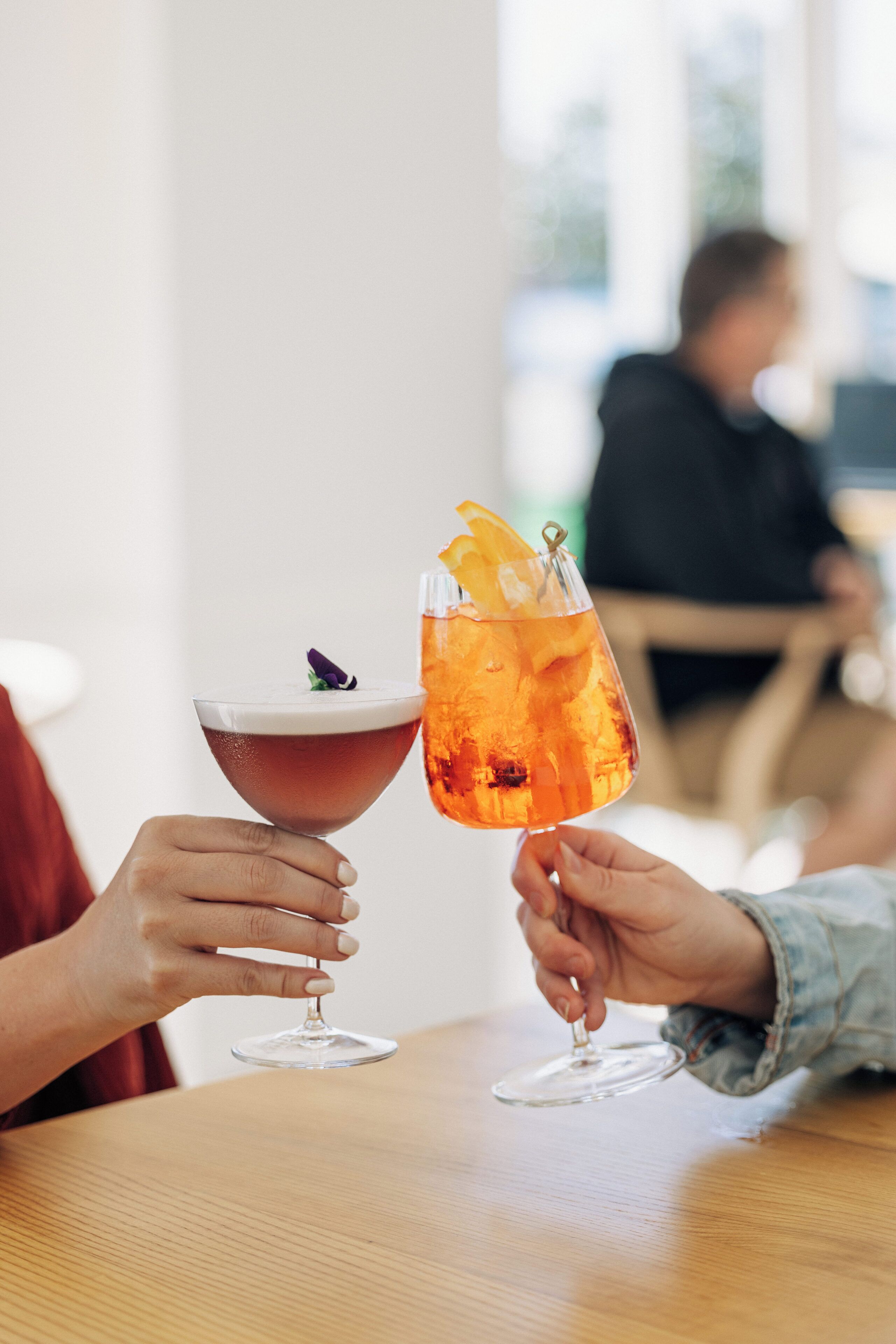 Two people holding cocktail glasses at a table.