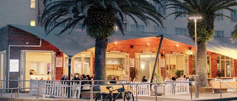 A hotel entrance with a covered patio area, palm trees, and a bicycle parked outside.