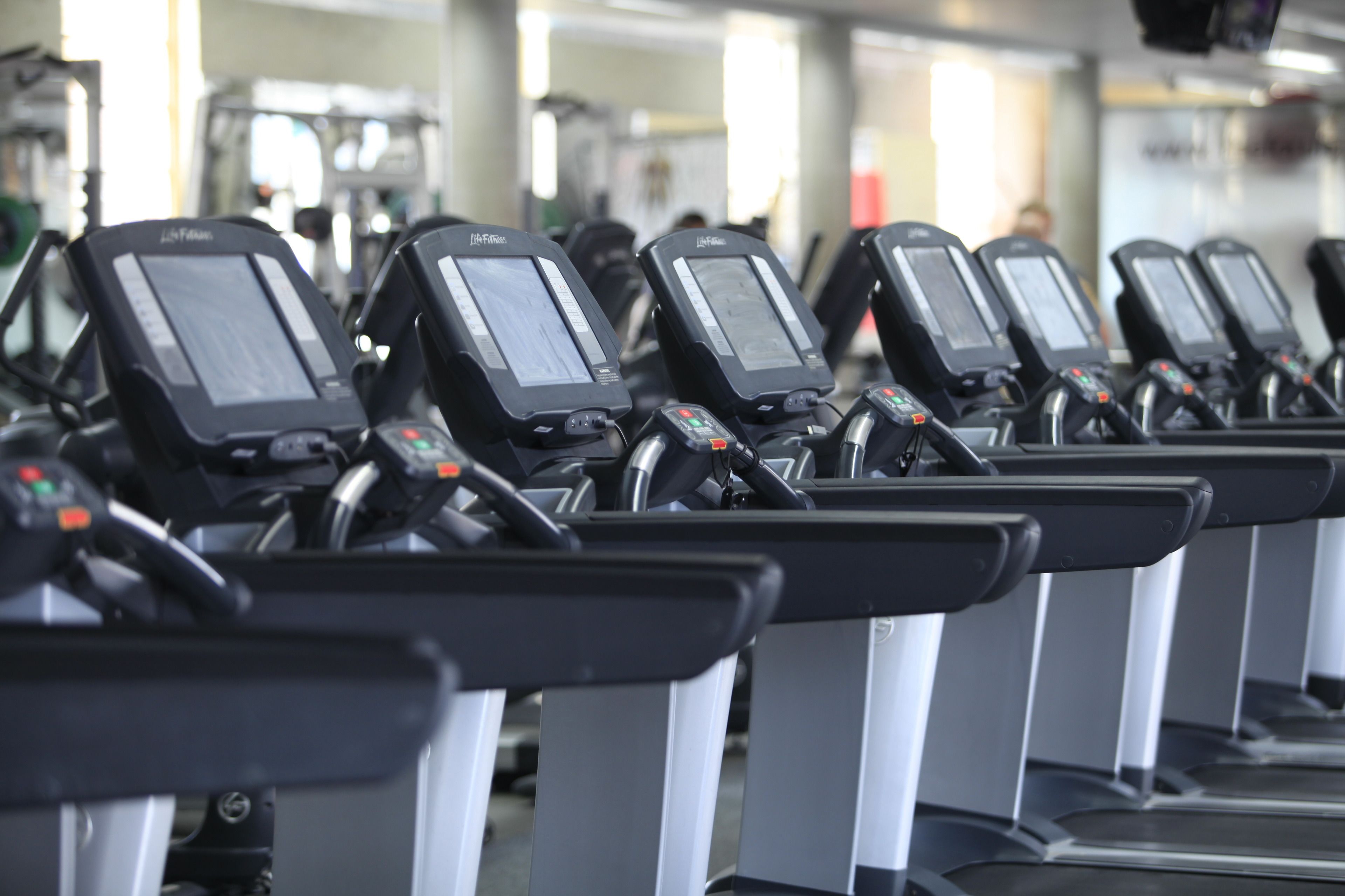 A row of stationary exercise bikes with digital displays, arranged in a gym setting.