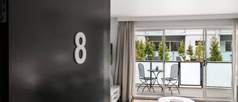A modern room with a large window, a balcony with outdoor furniture, and a round table.
