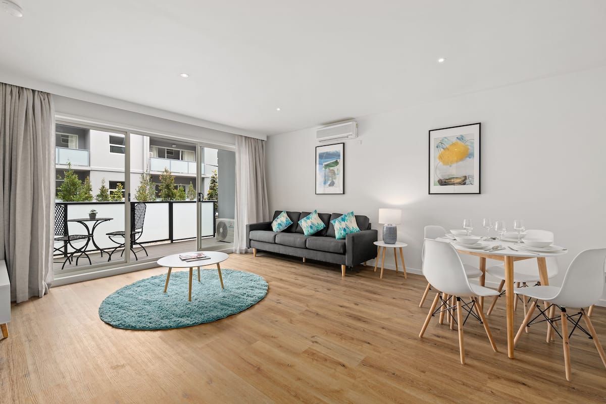 Un salon moderne avec un canapé gris, une table basse ronde et un coin repas comprenant des chaises blanches et une table en bois.