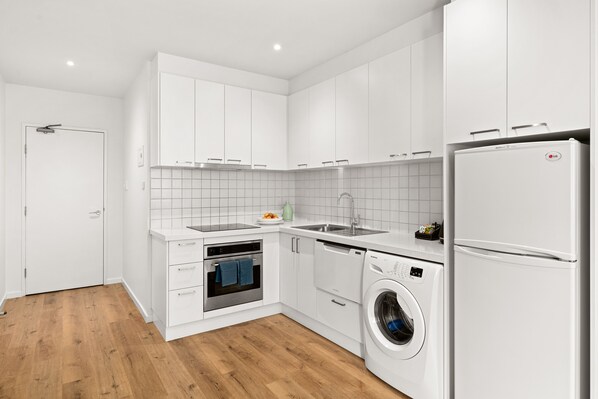 A modern kitchen with white cabinets, a built-in oven, a dishwasher, and a washing machine.
