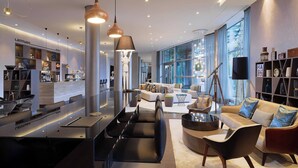 A modern interior with a kitchen area, seating with a sofa and chairs, and a large window providing natural light. - Le Méridien Hamburg (Hamburg)