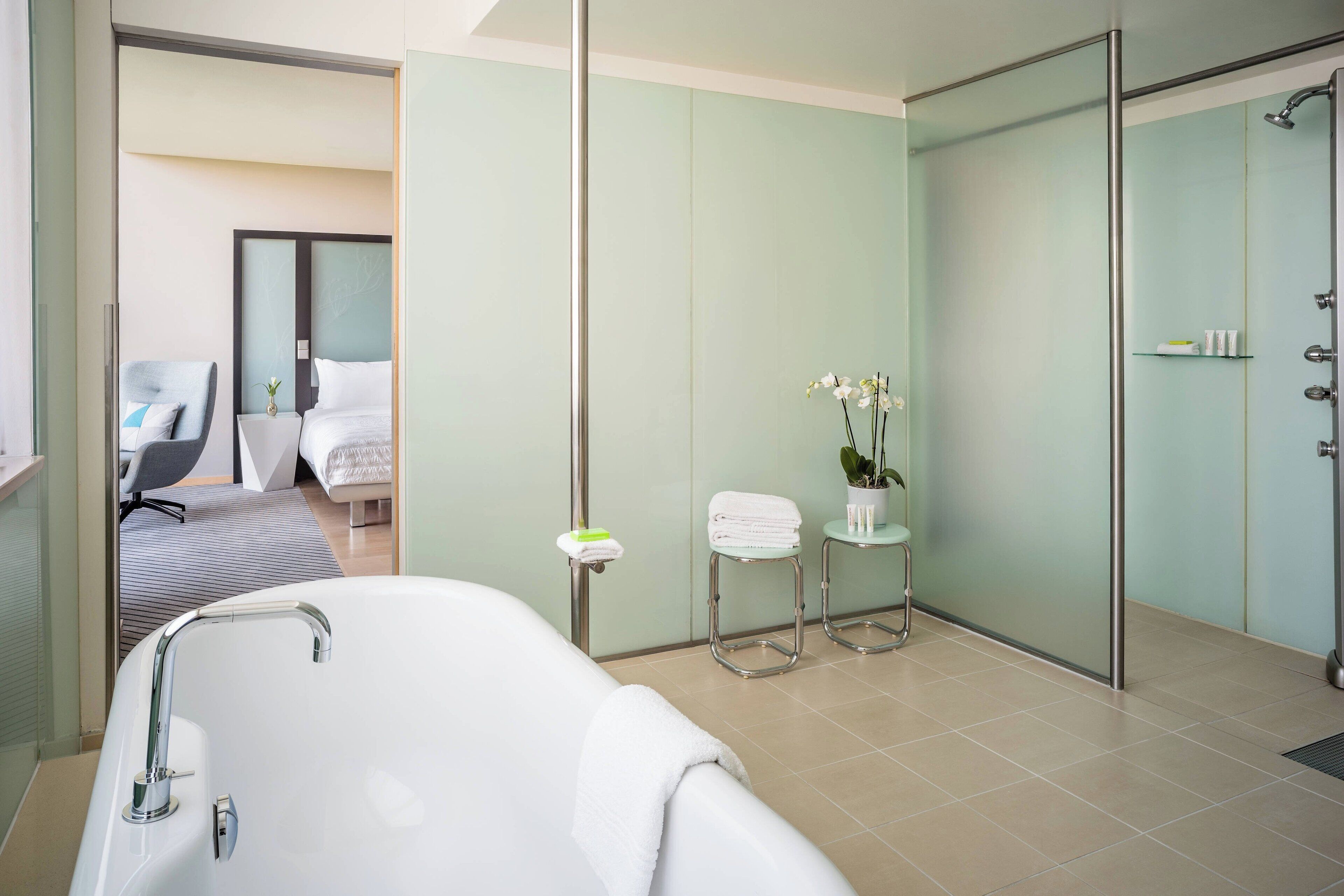 A modern bathroom with a bathtub, a shower, and a toilet. There is a chair and a small table with a plant.