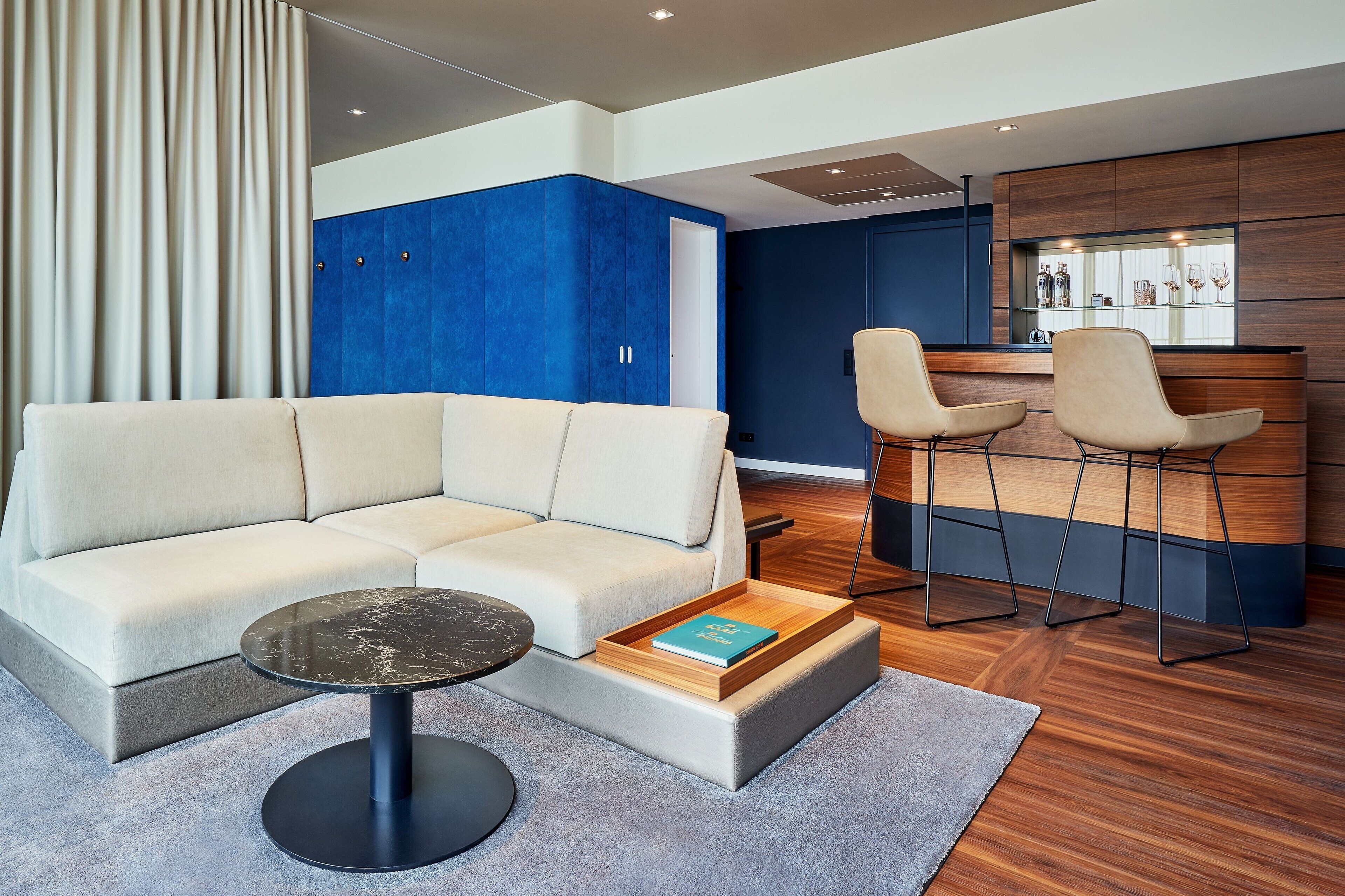 A modern living room with a sectional sofa, a round coffee table, and a bar area with two bar stools.