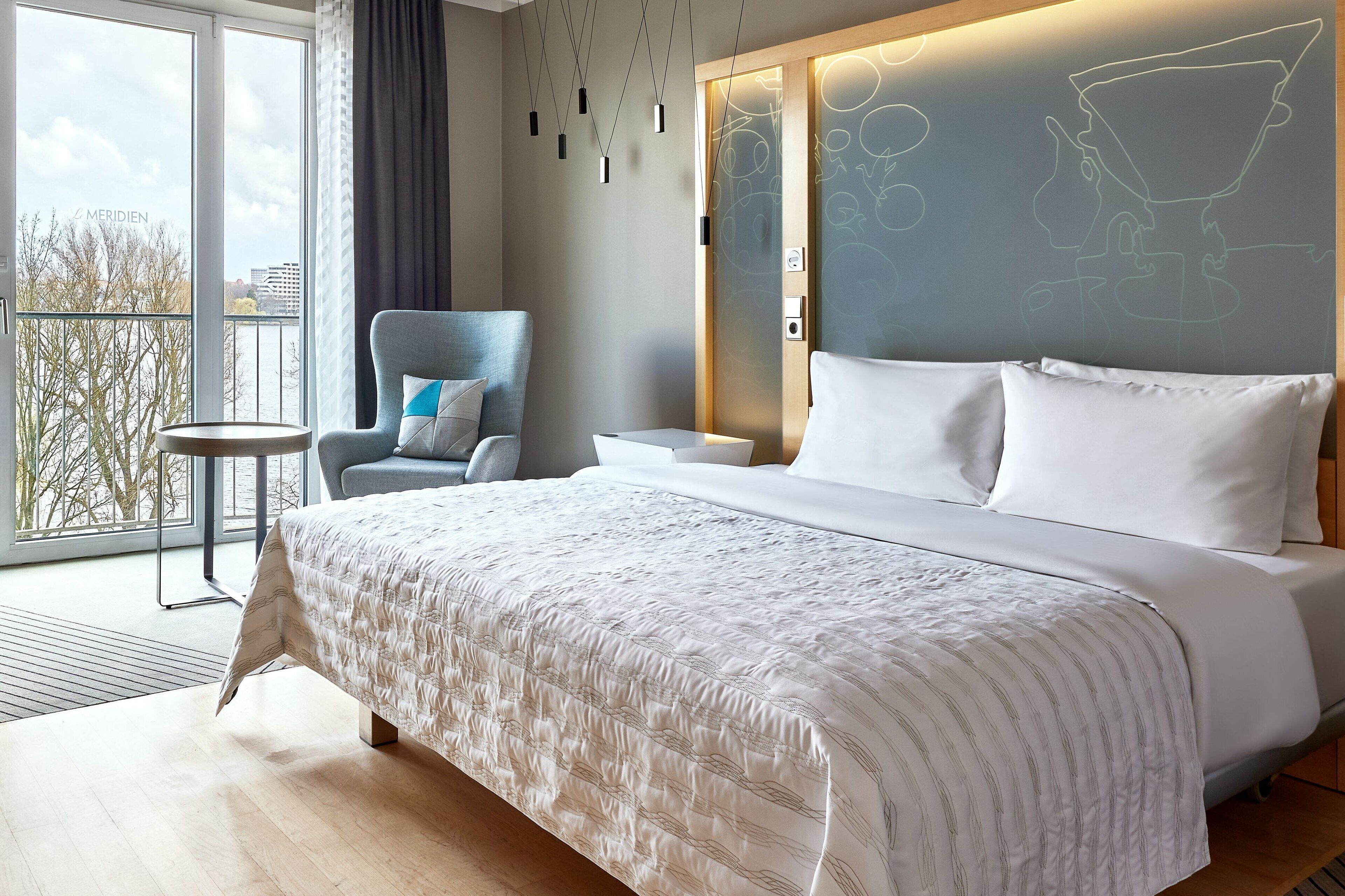 Une chambre d’hôtel moderne, dotée d’un grand lit, d’une chaise, d’une petite table et offrant une vue sur l’extérieur.
