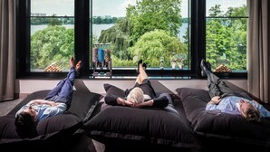 Three people lying on black bean bags in a room with large windows overlooking a lake and trees. - Le Méridien Hamburg (Hamburg)
