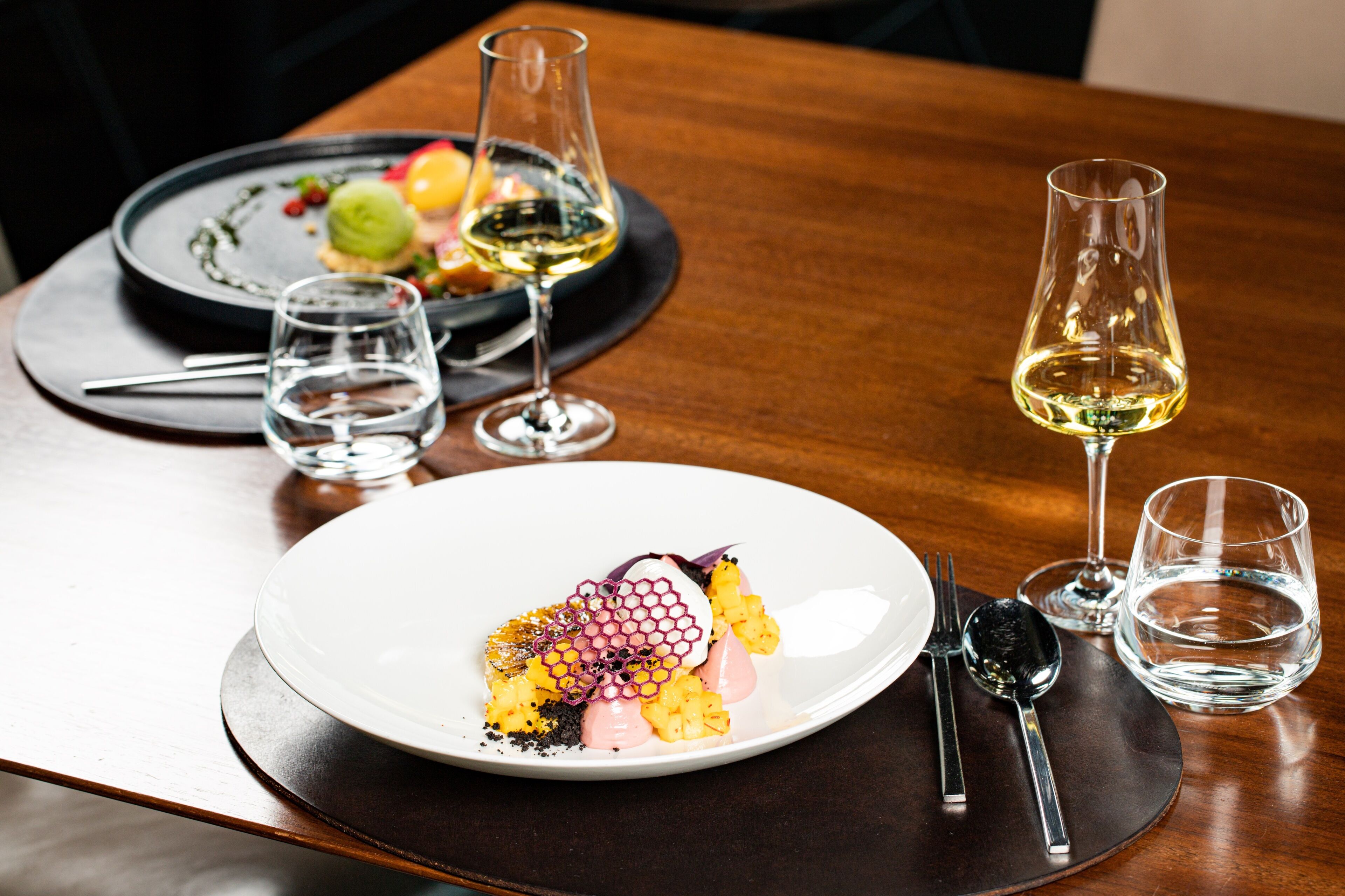 A dining table with a white plate of food, two wine glasses, and a water glass.