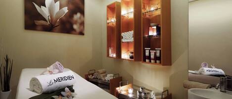 A hotel room with a bed, a large mirror, a vanity with a sink, and shelves with toiletries.