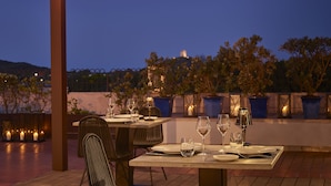 An outdoor dining area with tables set for two, featuring candlelit tables and potted plants.