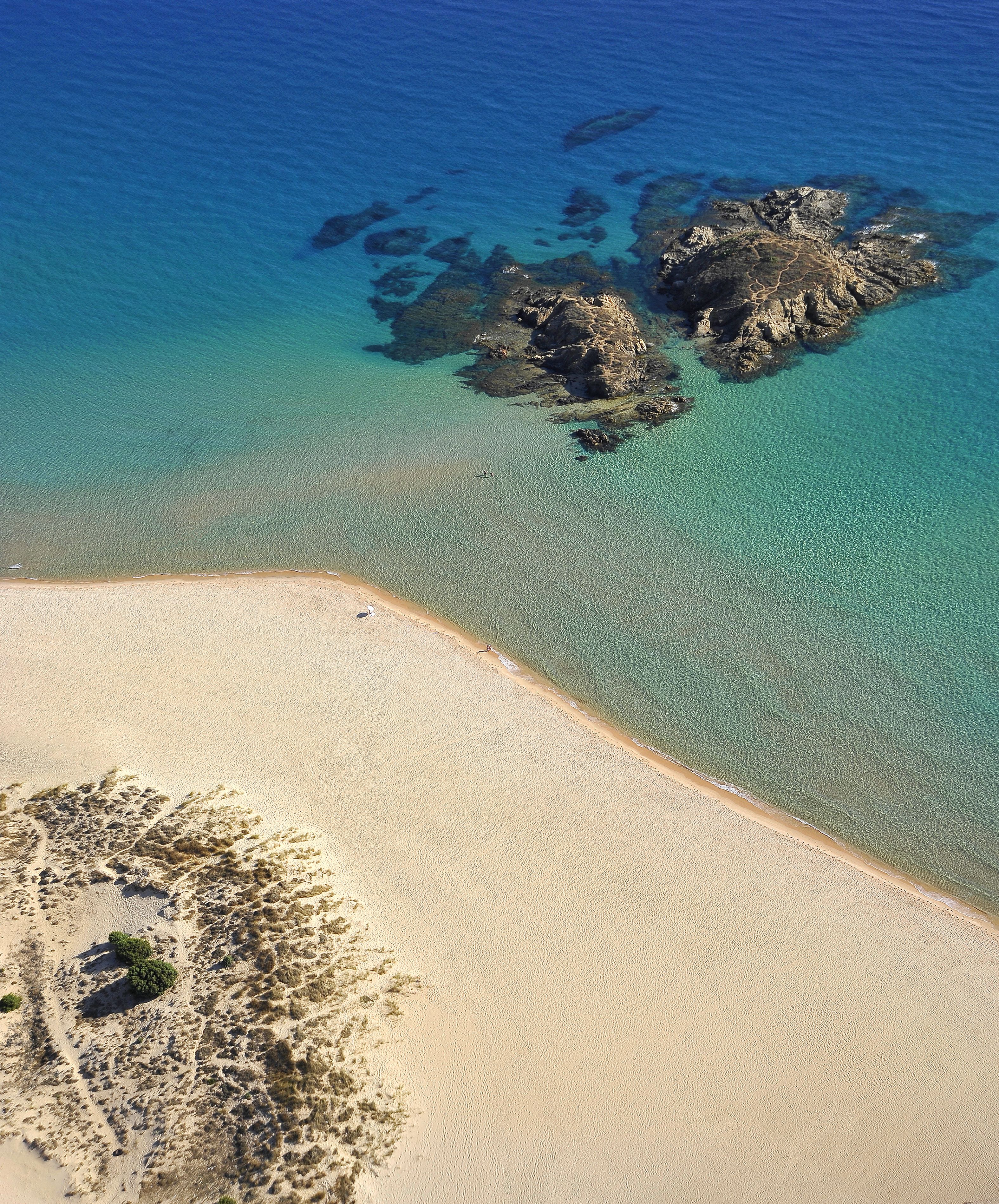 Vista aérea de una playa con aguas turquesas cristalinas, una orilla arenosa y afloramientos rocosos.