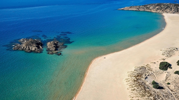 An aerial view of a beach with clear turquoise waters, a sandy shore, and rocky outcrops.