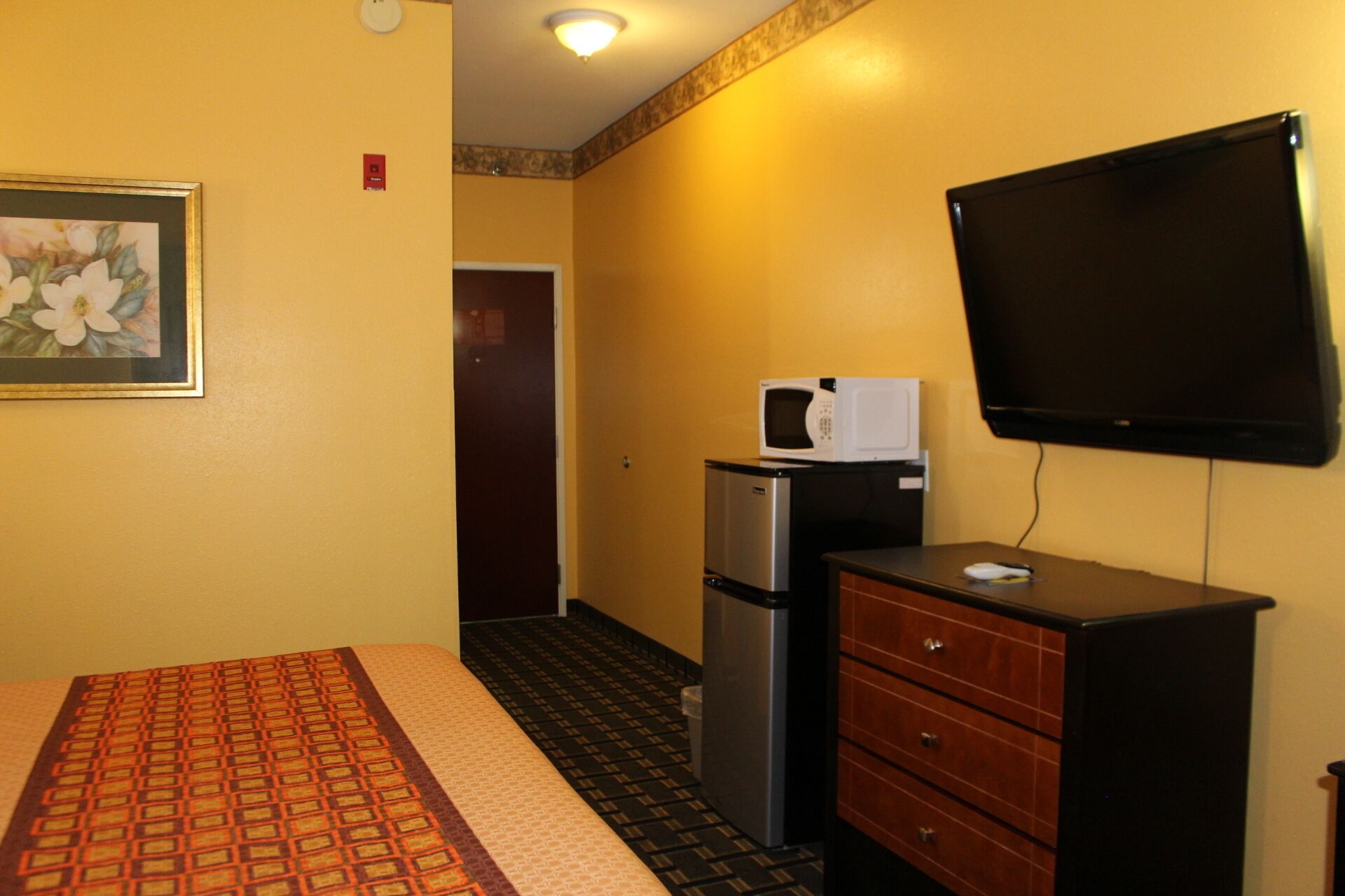 A hotel room with a bed, a dresser, a microwave, a refrigerator, and a television.