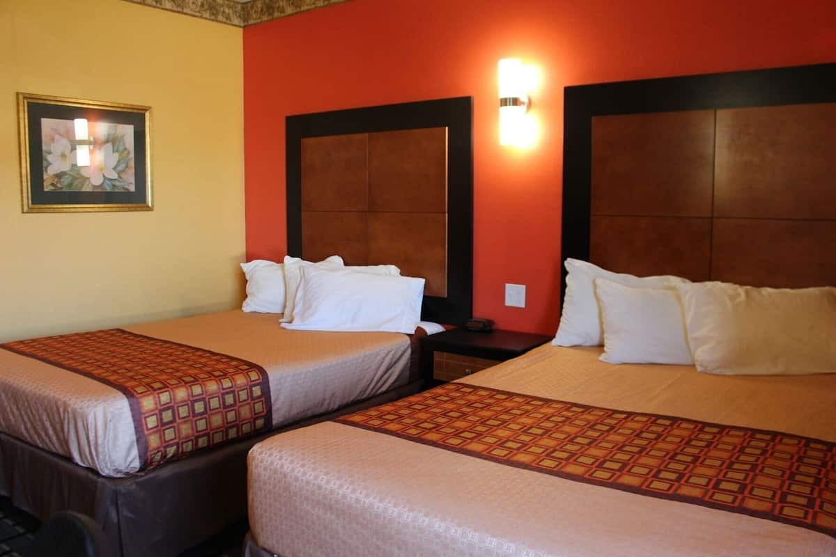 A hotel room with two beds, a nightstand, a wall-mounted light, and a framed picture.
