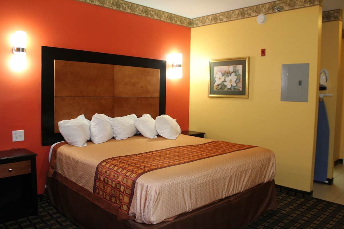 A hotel room with a large bed, a nightstand, a wall-mounted light, and a framed picture.